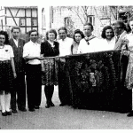 Gruppenfoto mit Menschen in historischen Kleidern, die eine Fahne halten, vor einem alten Gebäude.