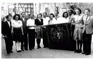 Gruppenfoto mit Menschen in historischen Kleidern, die eine Fahne halten, vor einem alten Gebäude.